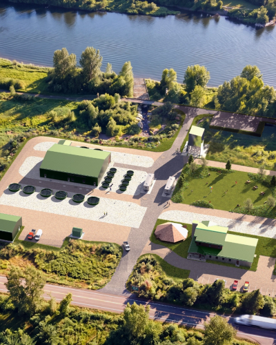 Aerial view of a modern facility with green buildings and circular tanks next to a river, surrounded by trees.