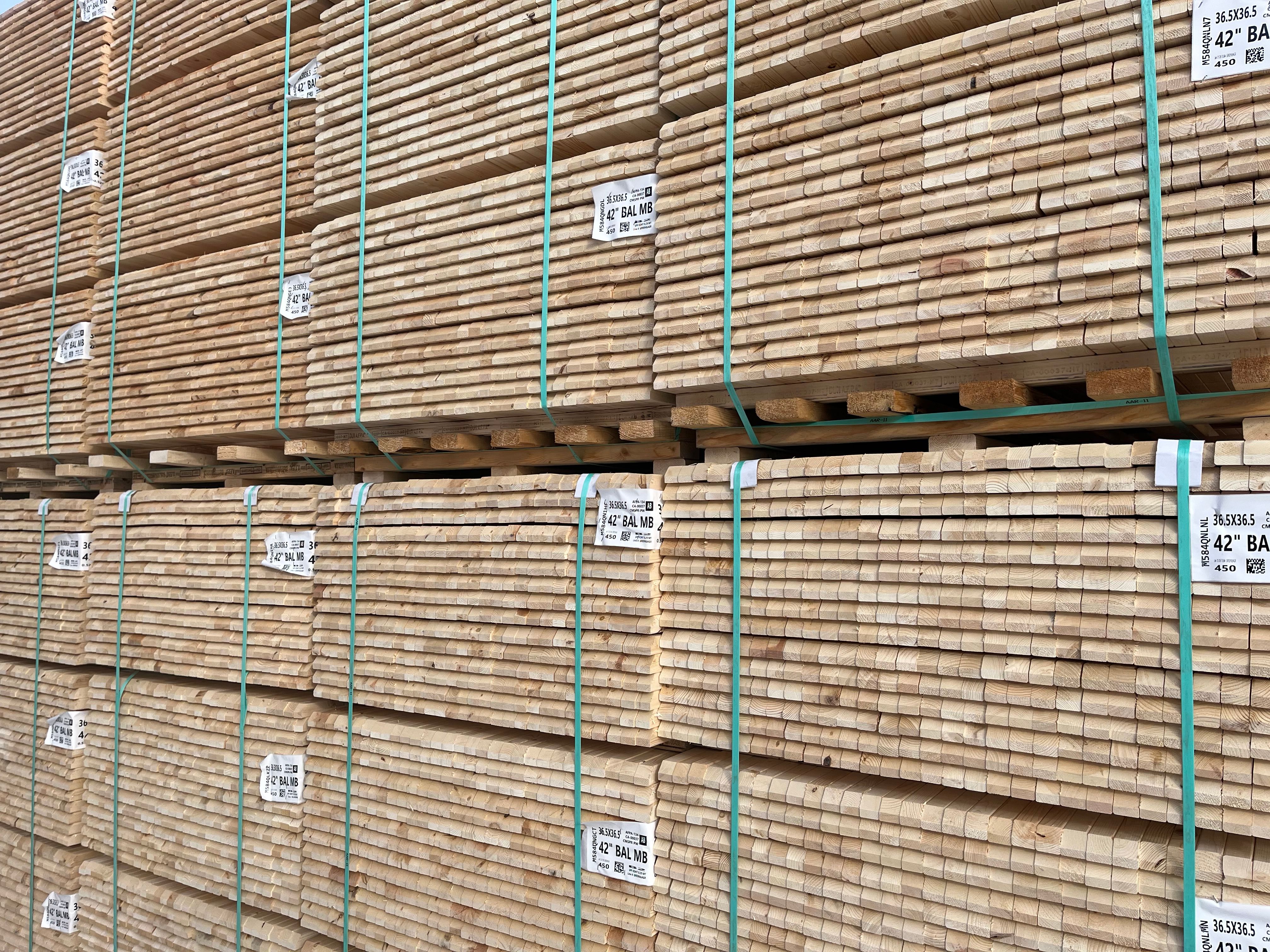 Large stacks of light-colored lumber planks bound with green straps.