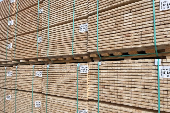 Large stacks of light-colored lumber planks bound with green straps.