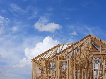 Wooden house frame under construction against a blue, cloudy sky.
