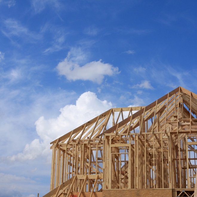 Wooden house frame under construction against a blue, cloudy sky.