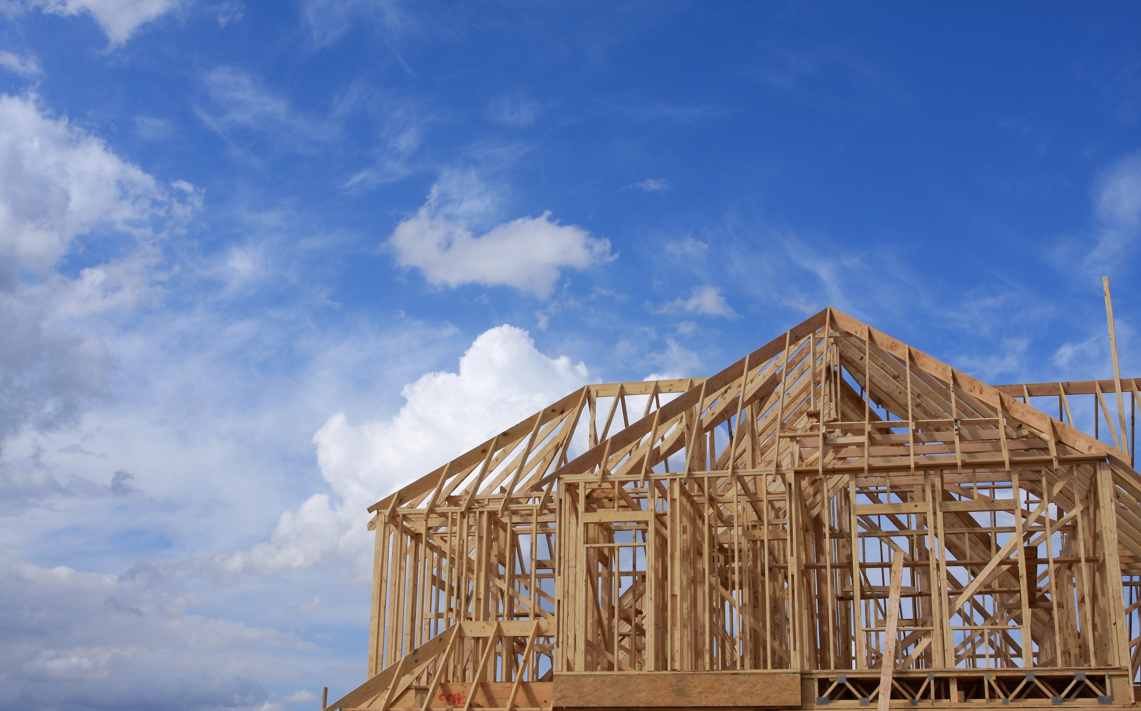 Wooden frame of a house under construction against a blue sky with white clouds.