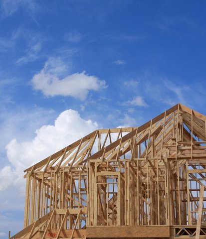 Wooden frame of a house under construction against a blue sky with white clouds.