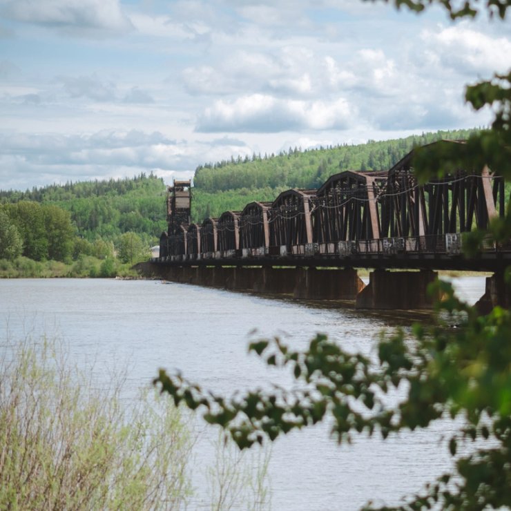 a train bridge over a river with trees in the foreground .