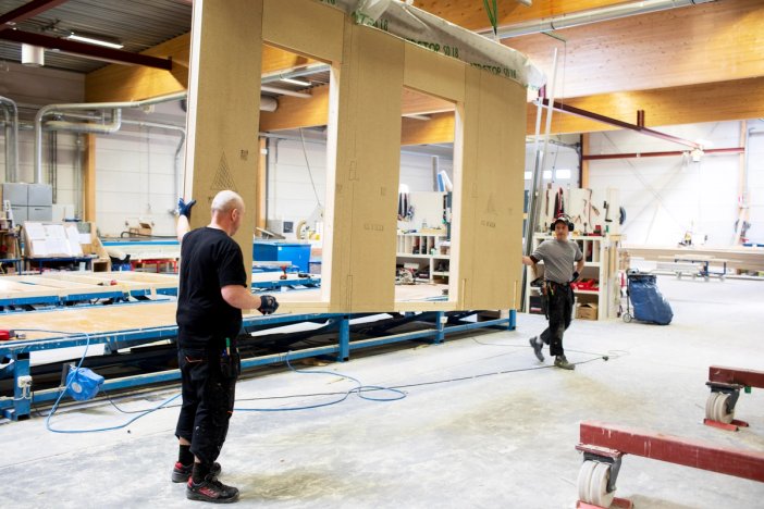 two men are working on a wooden wall in a factory prefabricated wall in a factory.