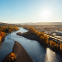 A winding river separates autumn trees from a town under a bright, sunny sky.