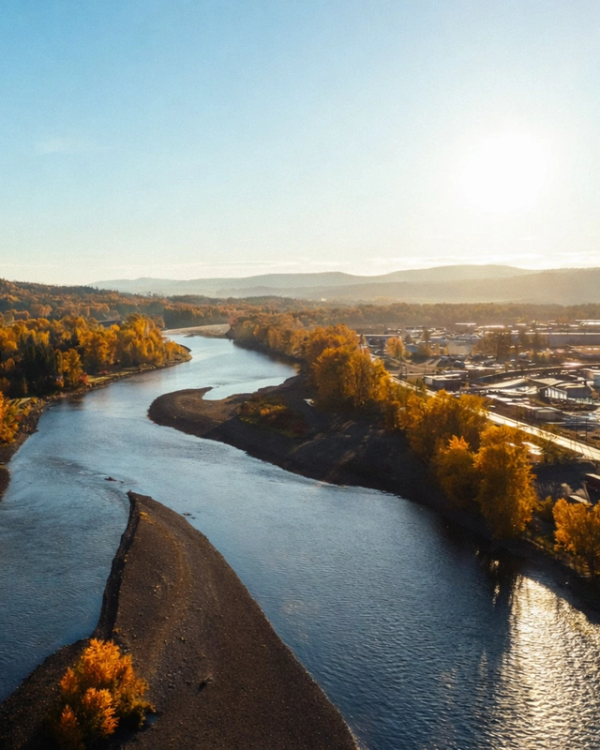 A winding river separates autumn trees from a town under a bright, sunny sky.