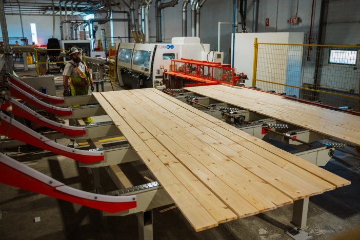 a man is standing next to a machine that is cutting wood in a factory .