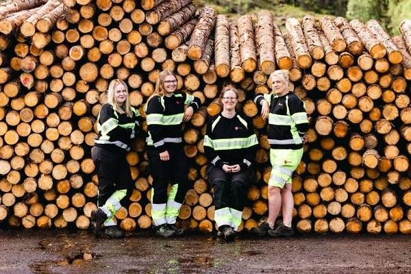 a group of women are posing for a picture in front of a pile of logs .