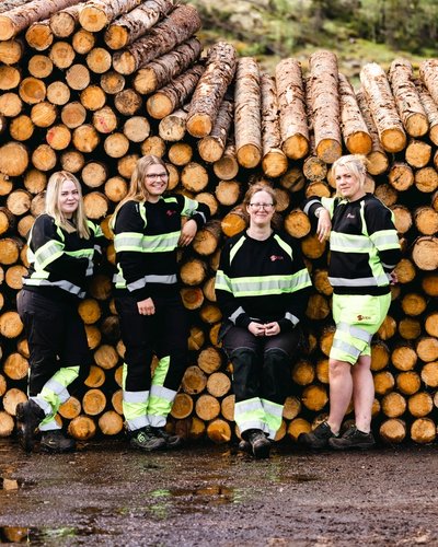 a group of women are posing for a picture in front of a pile of logs .