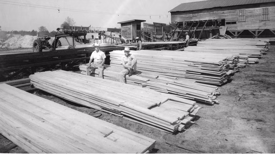 a black and white photo of two men sitting on a pile of wood