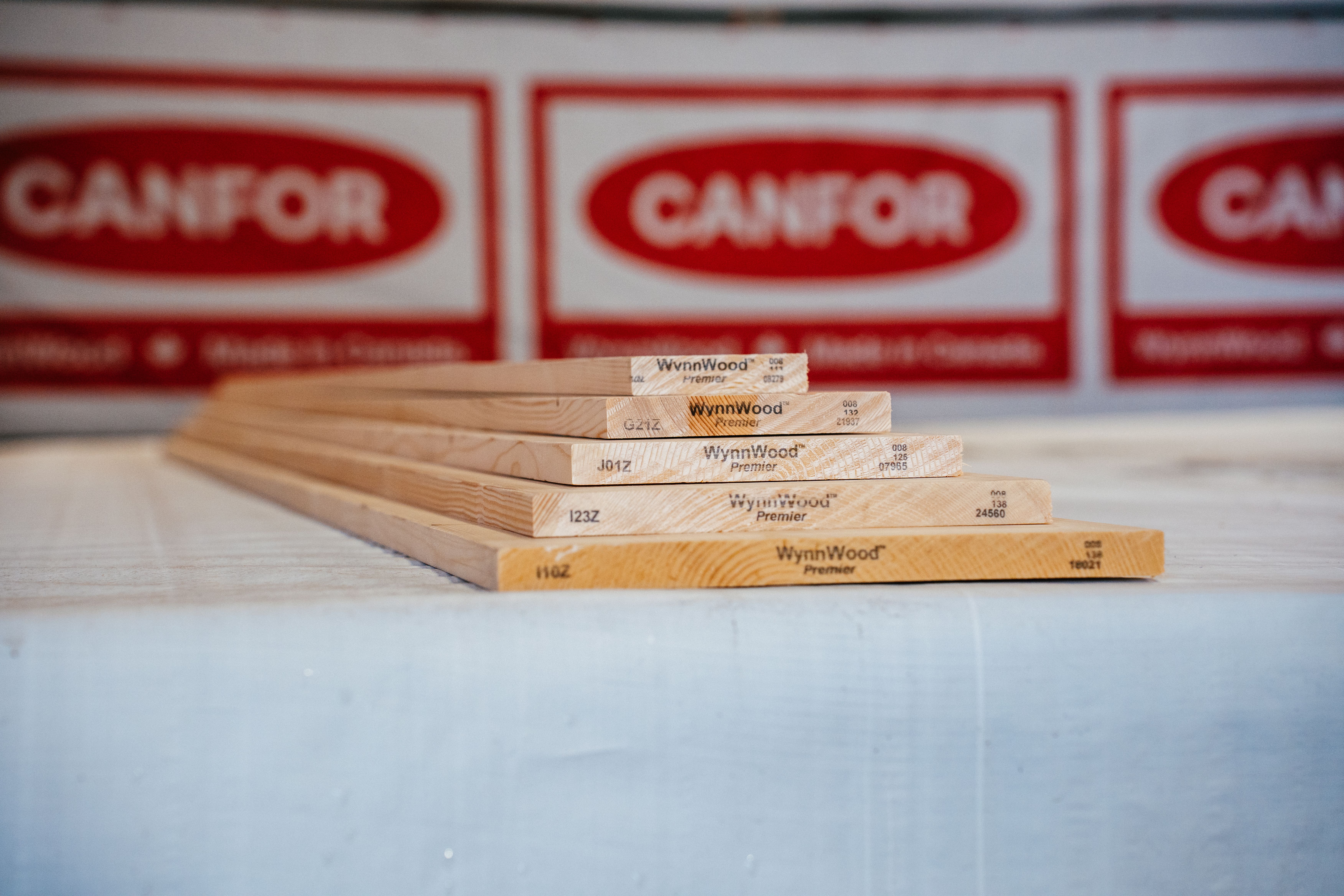 Five WynnWood Premier wooden boards laid on a surface, with blurred Canfor logos in the background.