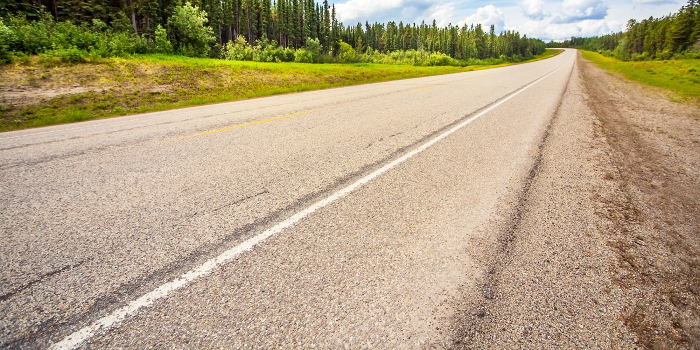an empty highway going through a forest on a cloudy day .