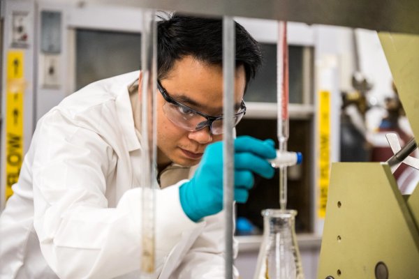 a man in a lab coat and gloves is working in a lab .
