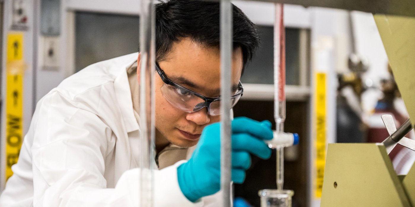 a man in a lab coat and gloves is working in a lab .