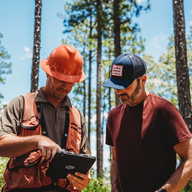 two men are looking at a tablet in the woods .