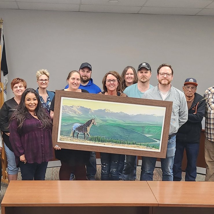 a group of people are standing around a table holding a painting of a horse .