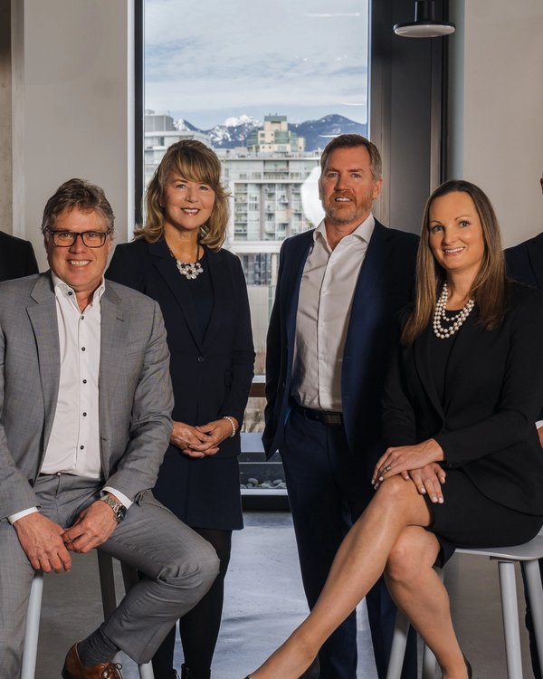 Six professionals in business attire in a modern office with city and mountain views.