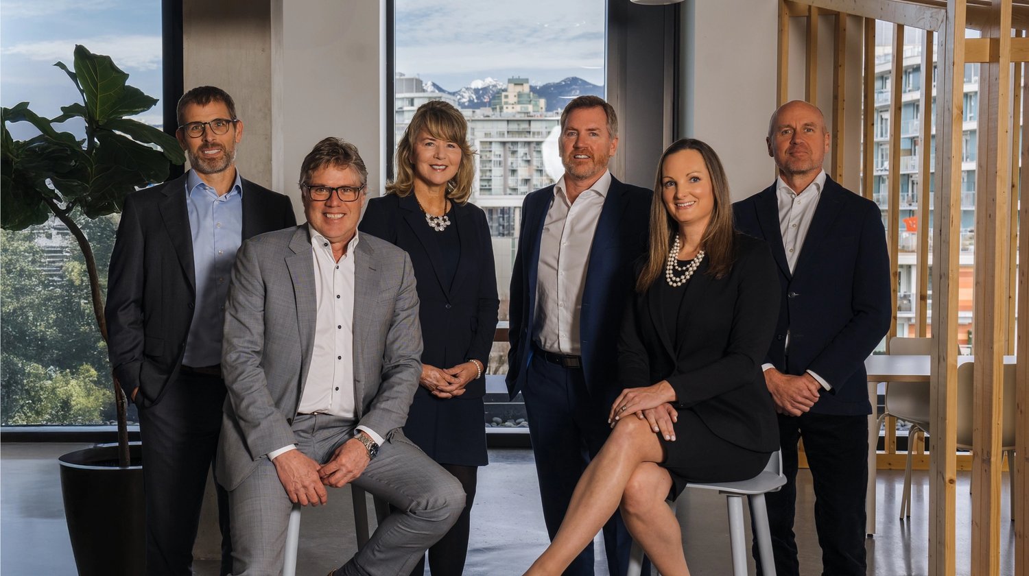 Six professionals in business attire in a modern office with city and mountain views.