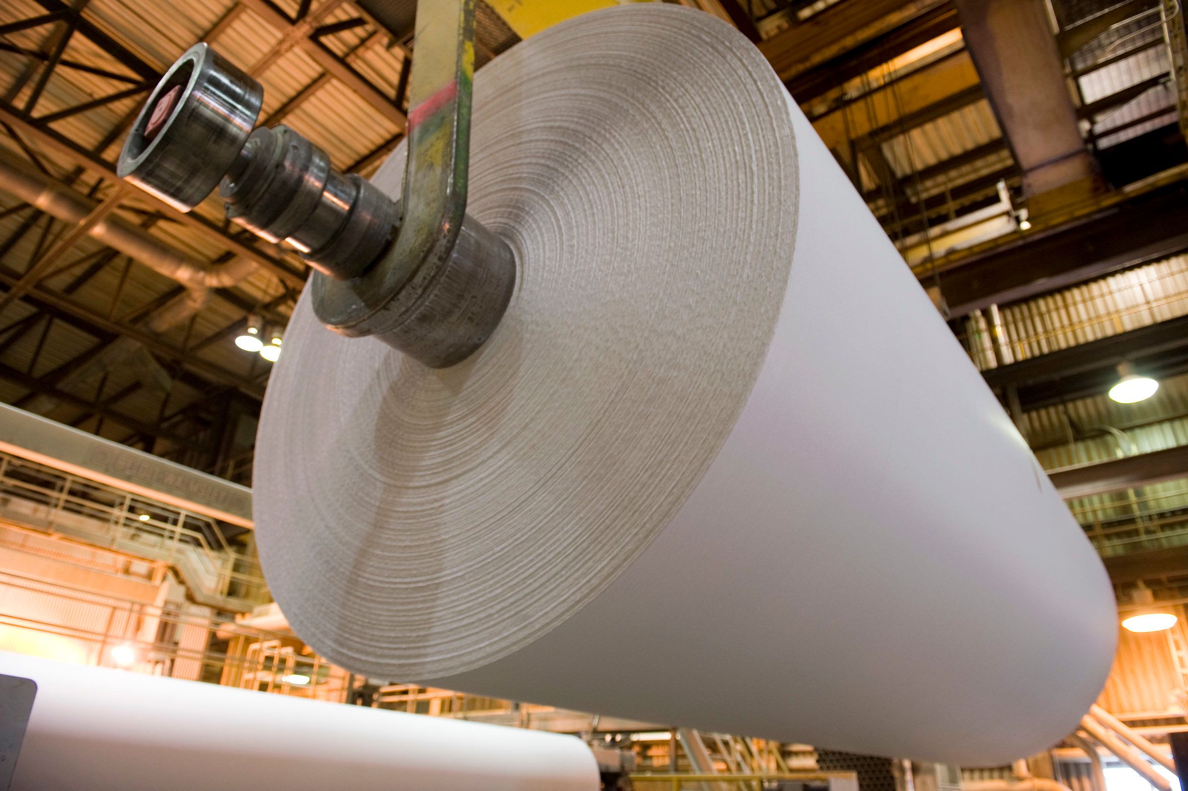 a roll of paper hangs from a lift inside a factory