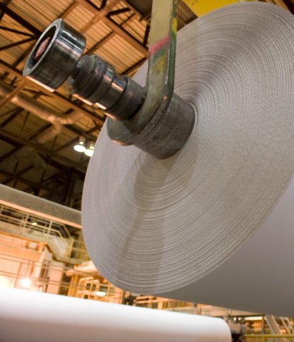 a roll of paper hangs from a lift inside a factory