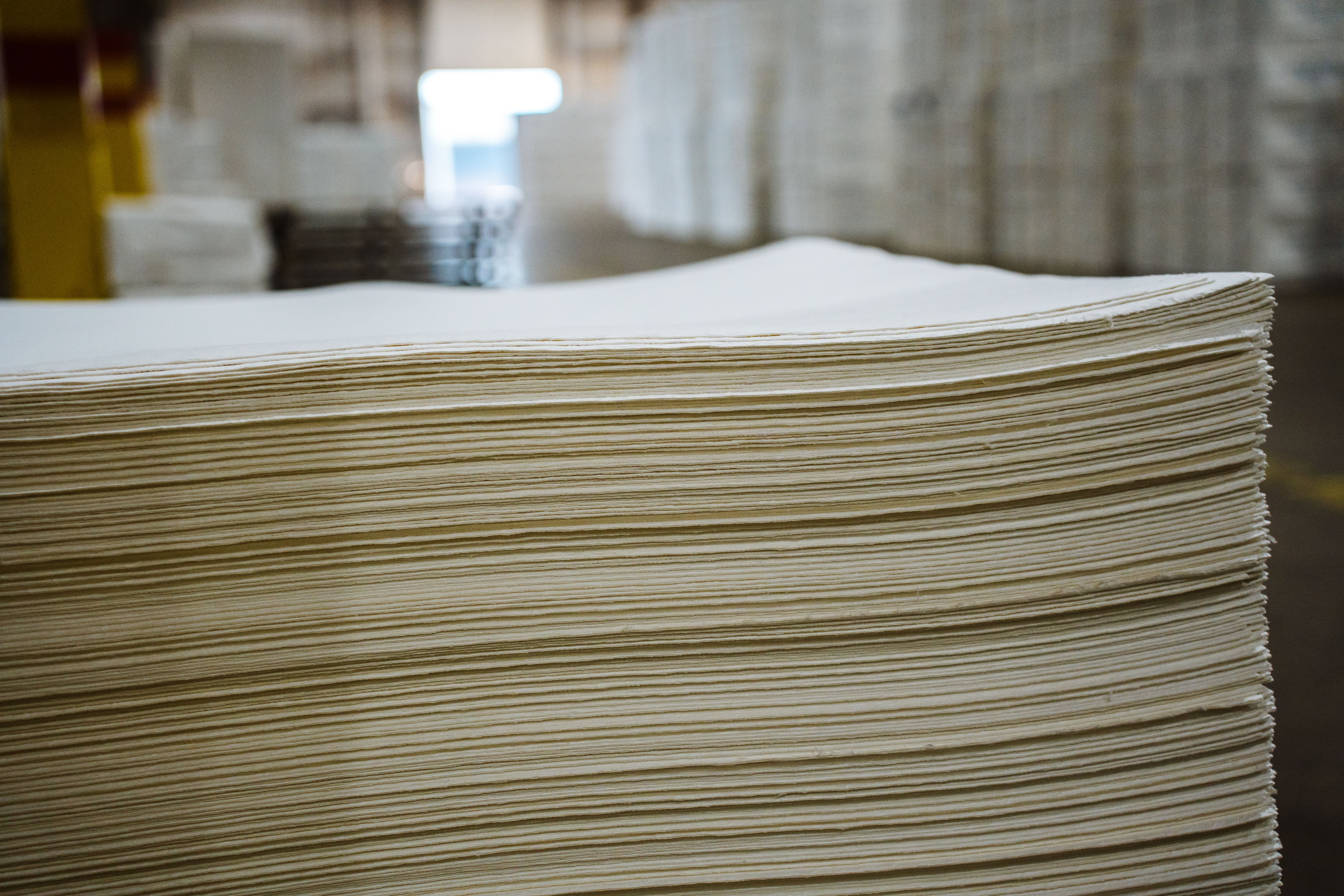 Side view of a large stack of light-colored paper sheets in a warehouse.
