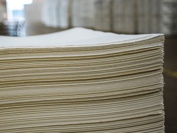 Side view of a large stack of light-colored paper sheets in a warehouse.