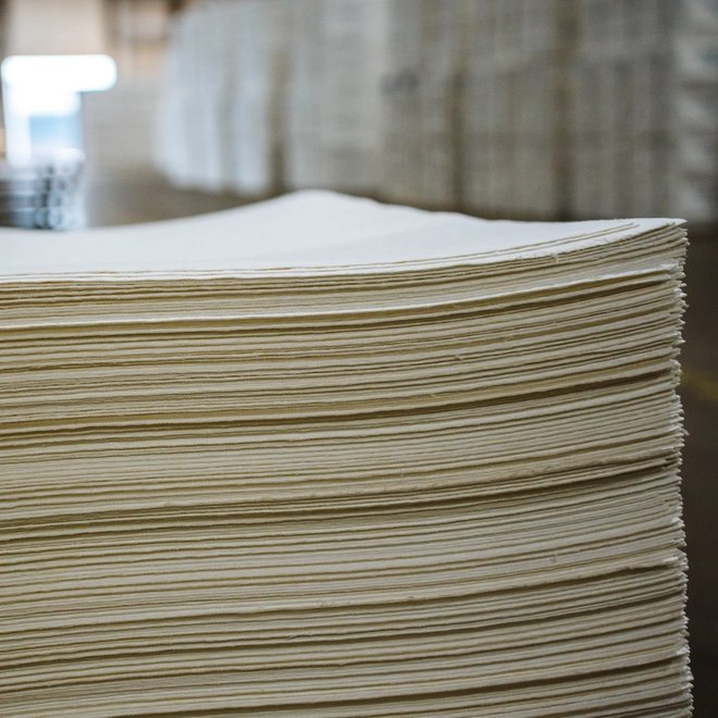 Side view of a large stack of light-colored paper sheets in a warehouse.