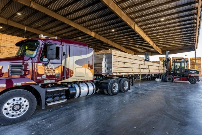 A NewSouth Express semi-truck with a lumber-loaded flatbed trailer alongside a forklift in a warehouse.