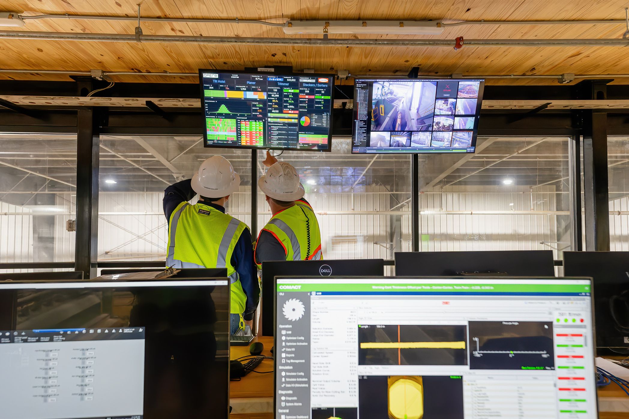 two construction workers are looking at a computer screen in a control room .