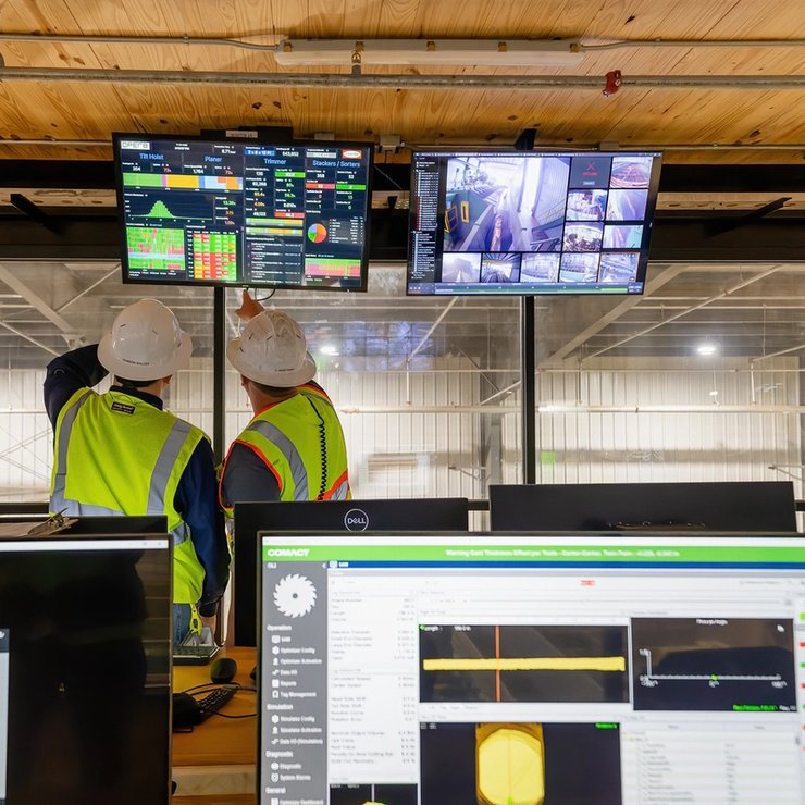 two construction workers are looking at a computer screen in a control room .