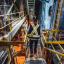 a man wearing a safety vest and hard hat is walking down a metal staircase at a pulp mill.