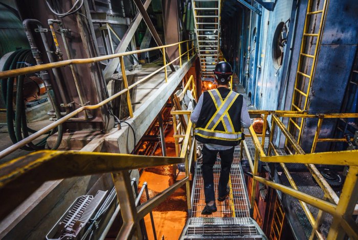 a man wearing a safety vest and hard hat is walking down a metal staircase at a pulp mill.