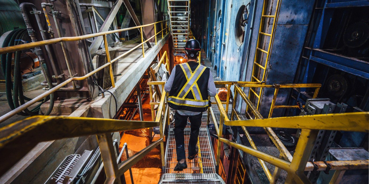 a man wearing a safety vest and hard hat is walking down a metal staircase at a pulp mill.