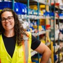 a woman wearing a yellow vest and glasses is standing in a warehouse .