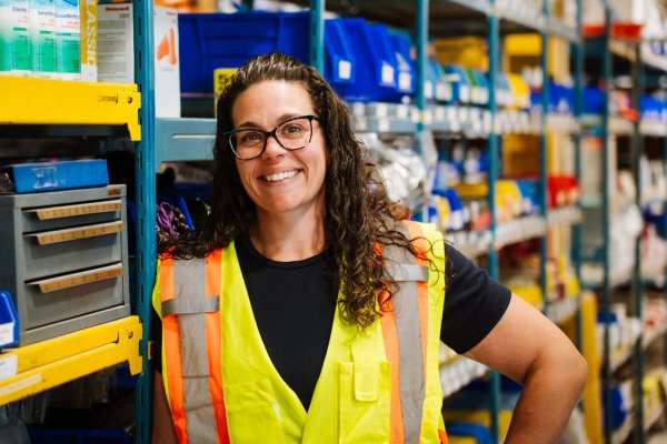 a woman wearing a yellow vest and glasses is standing in a warehouse .