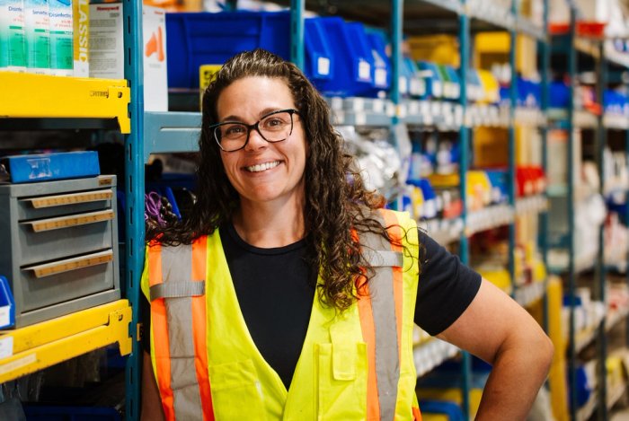 a woman wearing a yellow vest and glasses is standing in a warehouse .