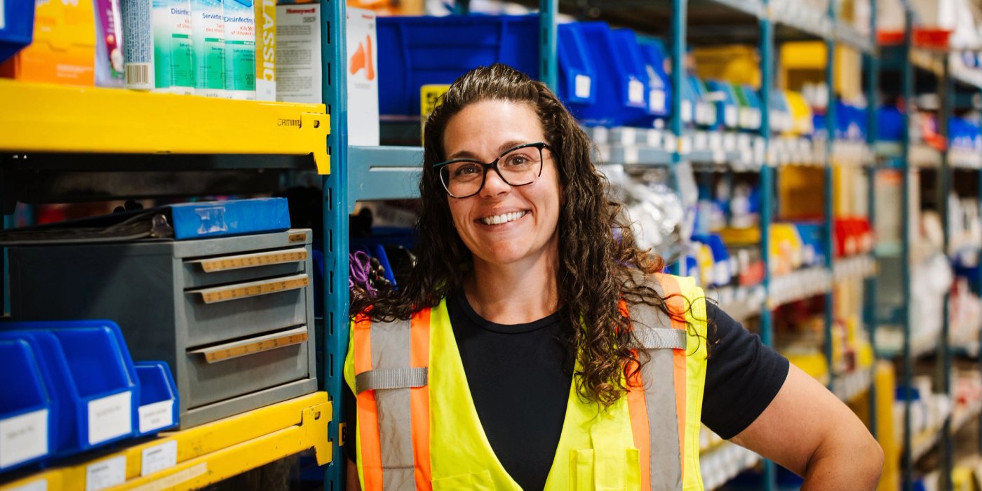 a woman wearing a yellow vest and glasses is standing in a warehouse .