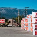 a semi truck is carrying a trailer with stacks of Canfor lumber out of a lumber yard.