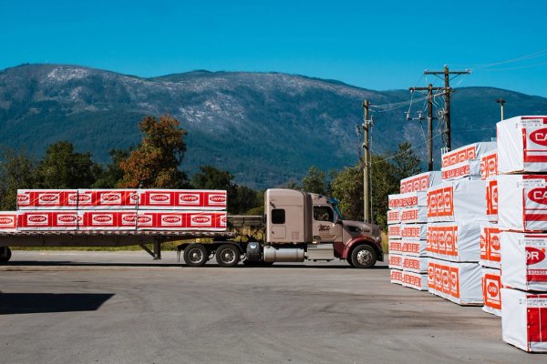 a semi truck is carrying a trailer with stacks of Canfor lumber out of a lumber yard.