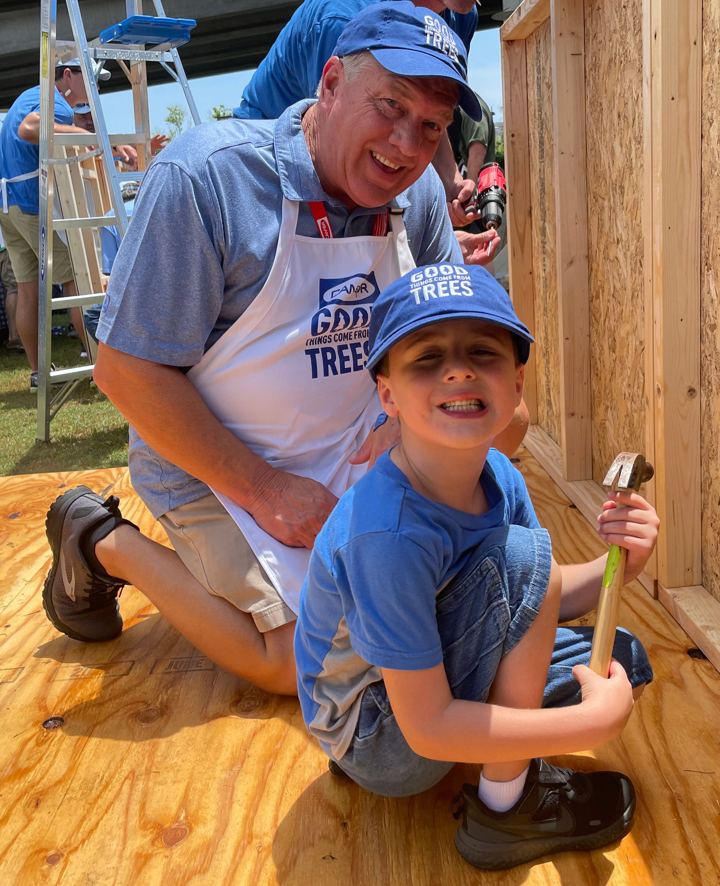 a man is kneeling down next to a little boy holding a hammer .