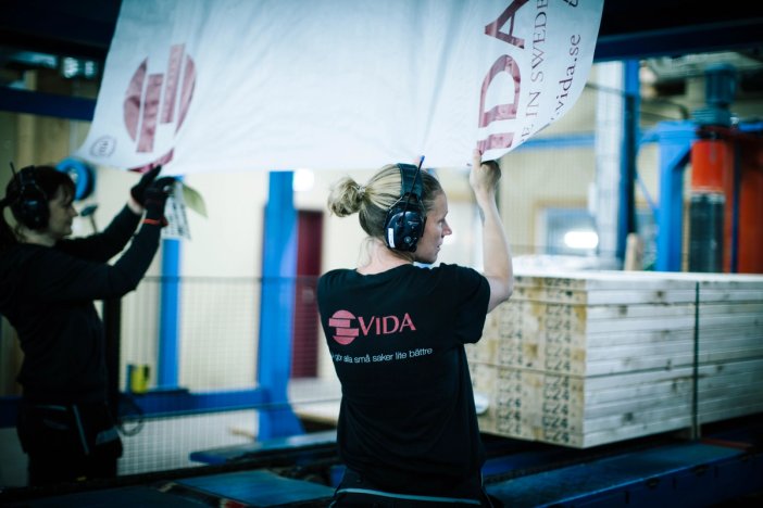 a woman wearing ear protection is wrapping lumber in a factory .