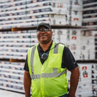 A smiling man in a safety vest stands beside stacked Canfor Power Products.