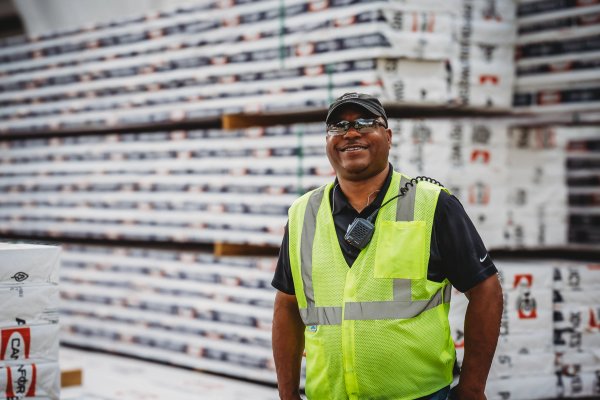 A smiling man in a safety vest stands beside stacked Canfor Power Products.