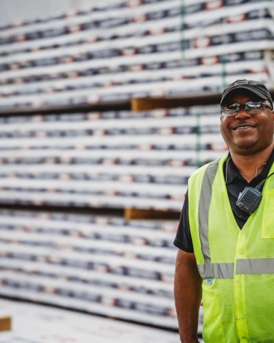 A smiling man in a safety vest stands beside stacked Canfor Power Products.