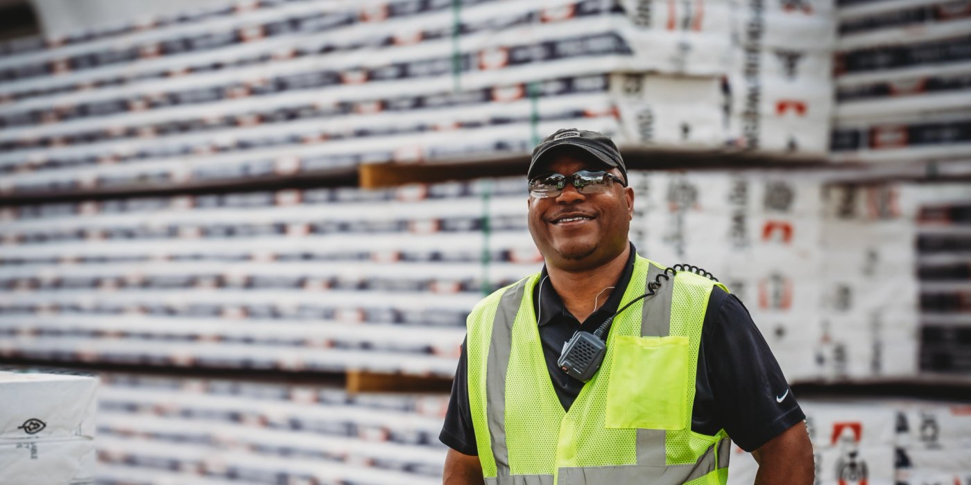 A smiling man in a safety vest stands beside stacked Canfor Power Products.