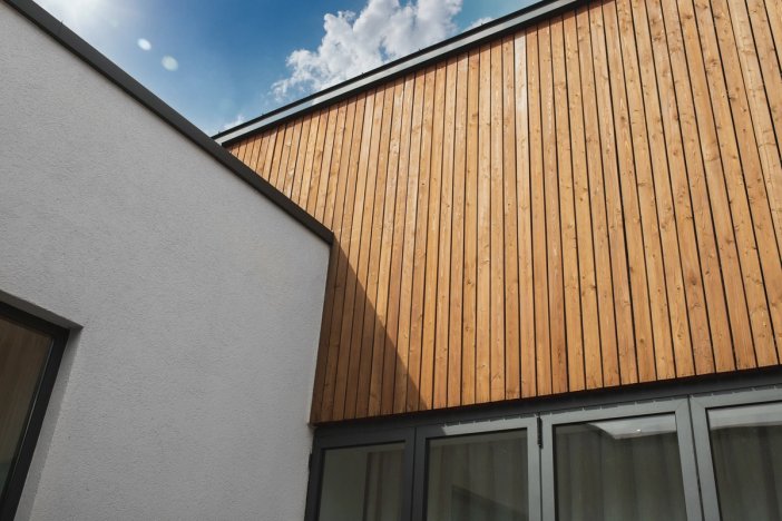 Modern building exterior with white stucco and vertical wood siding under a blue sky.