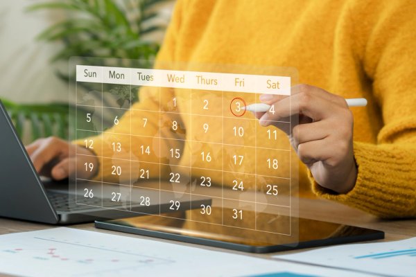 a person is looking at a calendar on a tablet while using a laptop .