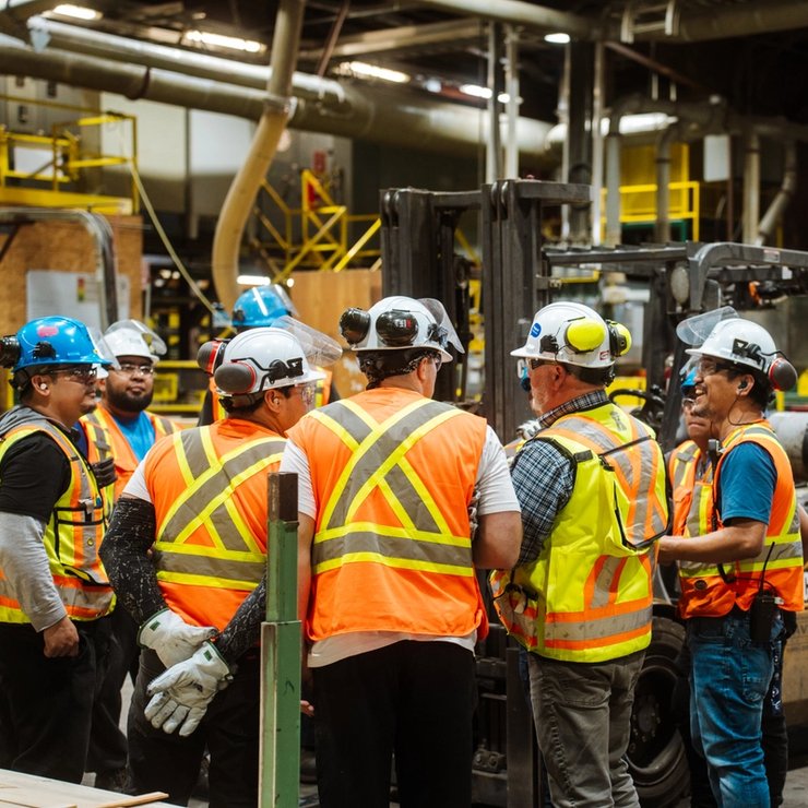 a group of construction workers are standing around a forklift in a factory .