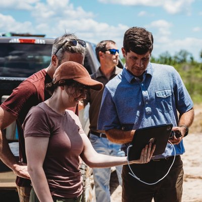 a group of people are standing in front of a truck looking at a tablet .